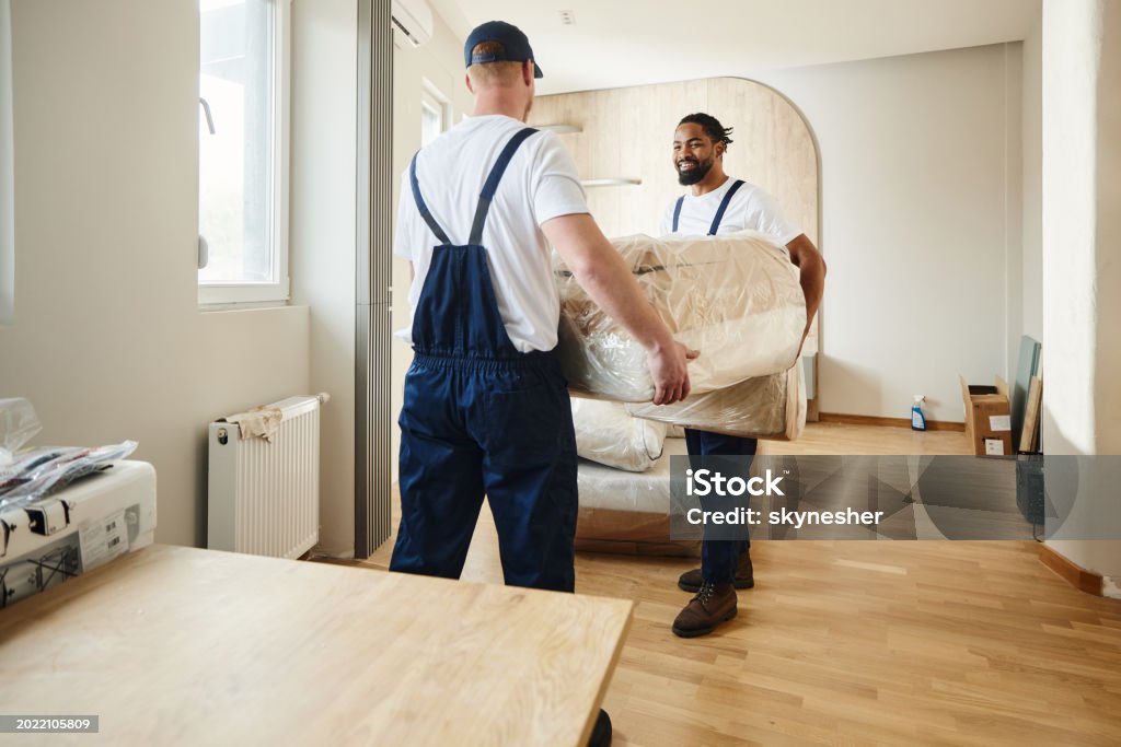 Two happy workers cooperating while carrying furniture into a new apartment.